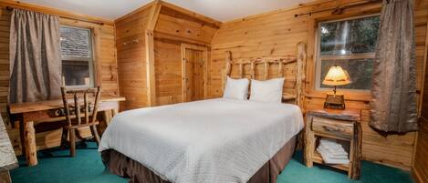 A wooden cabin room with a bed, a desk, and a lamp.
