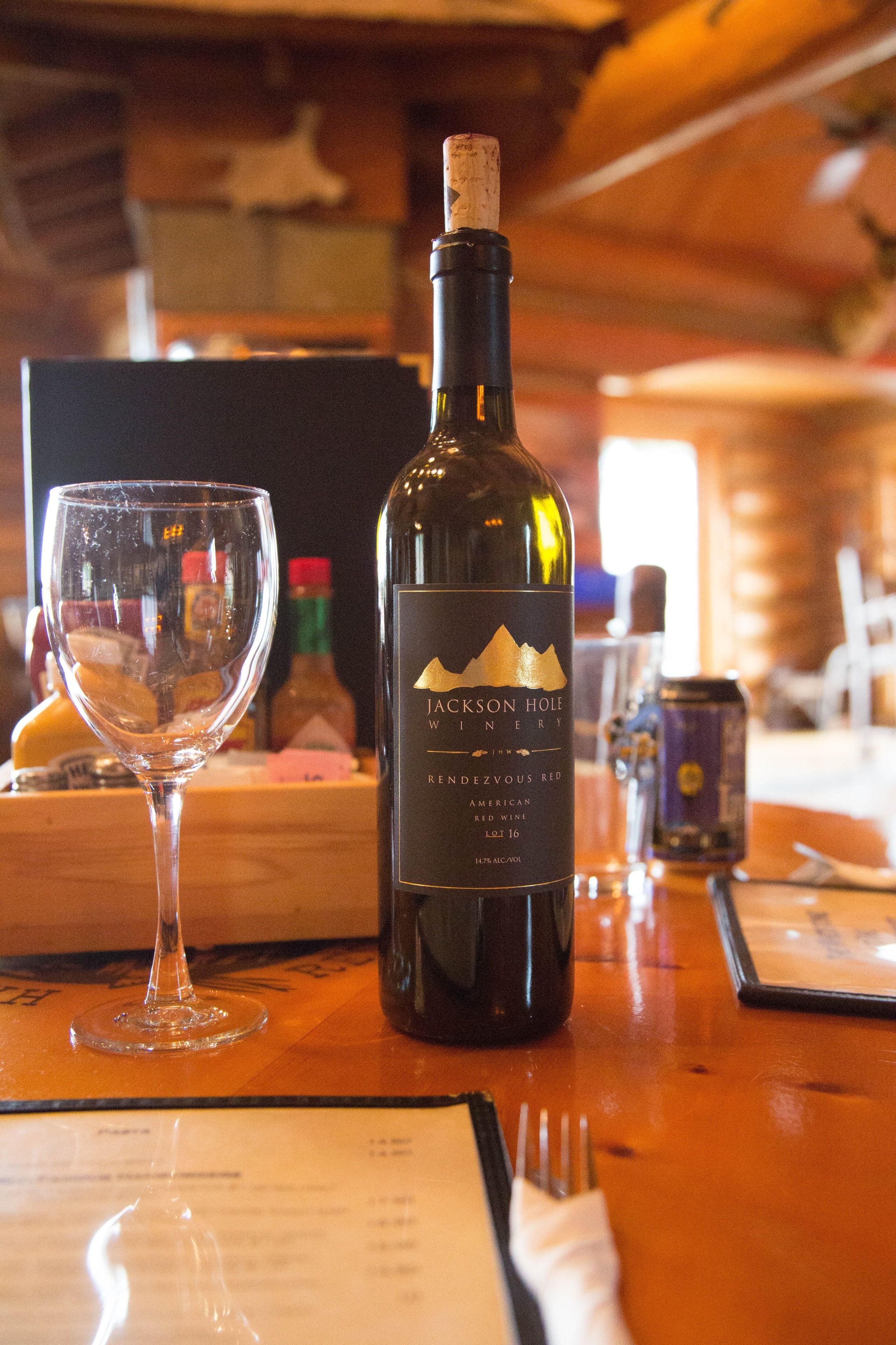 A bottle of Jackson Hole Winery Reserve Red wine and a wine glass on a wooden table.
