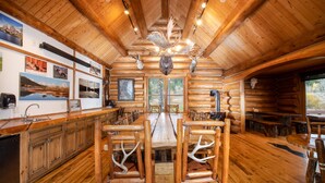 A log cabin interior with a wooden dining table, benches with antler backrests, a kitchen area, and framed pictures on the walls. - Hatchet Resort (Moran)