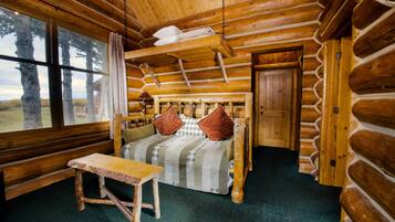 Een slaapkamer in een blokhut met een bed, een tafel en een raam met uitzicht op een bos.