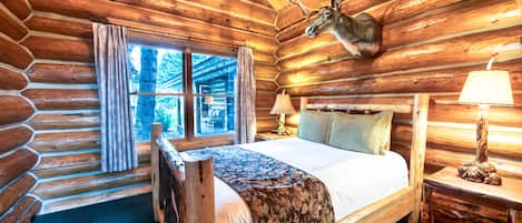 Een slaapkamer in een blokhut met een bed, een opgezette hertenkop aan de muur en een raam met gordijnen.