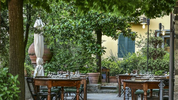 An outdoor dining area with tables and chairs, surrounded by greenery and a stone pathway. - Hotel Bellavista Impruneta (Impruneta)