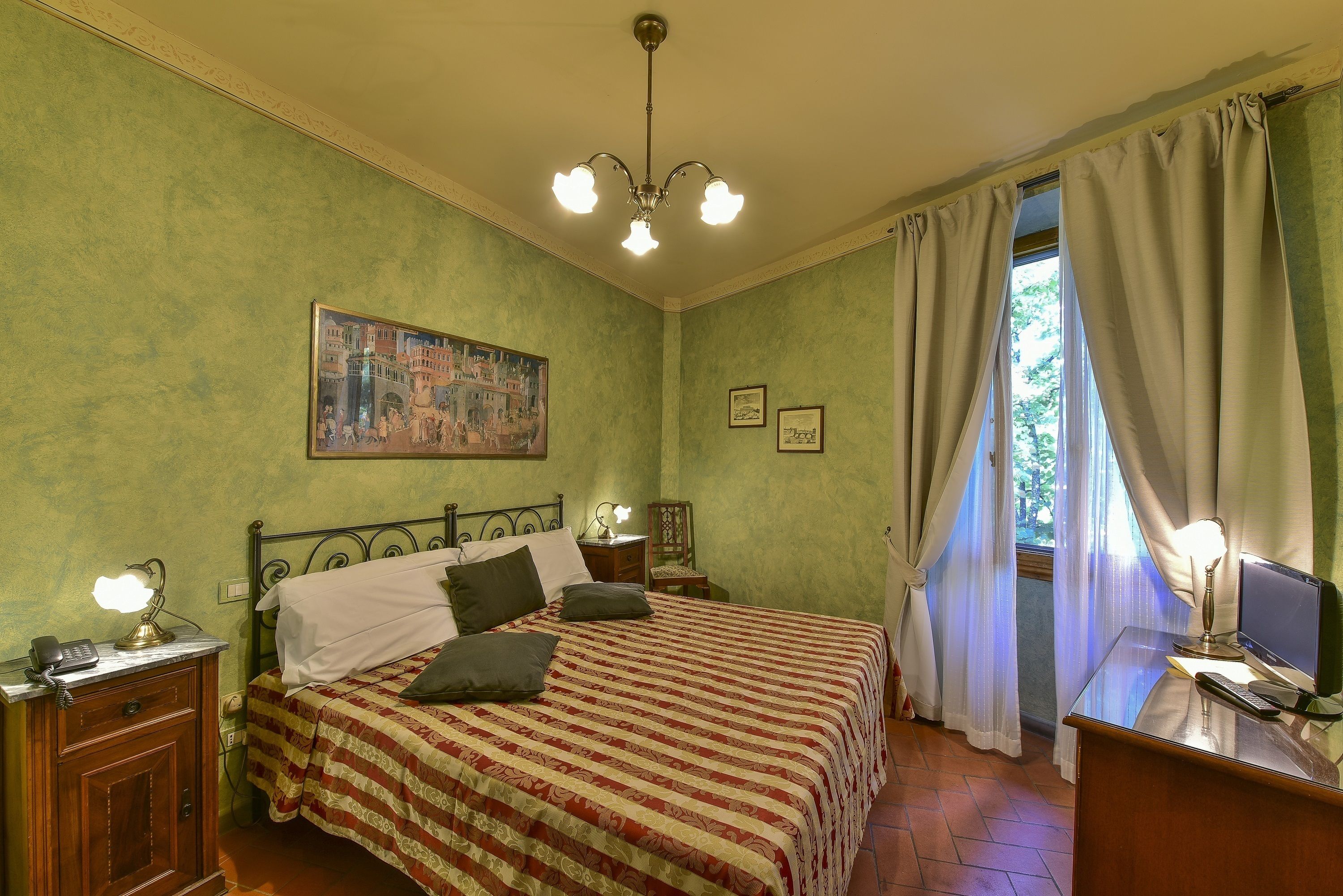 A bedroom with a bed, bedside lamps, a desk with a computer, and a window with curtains.