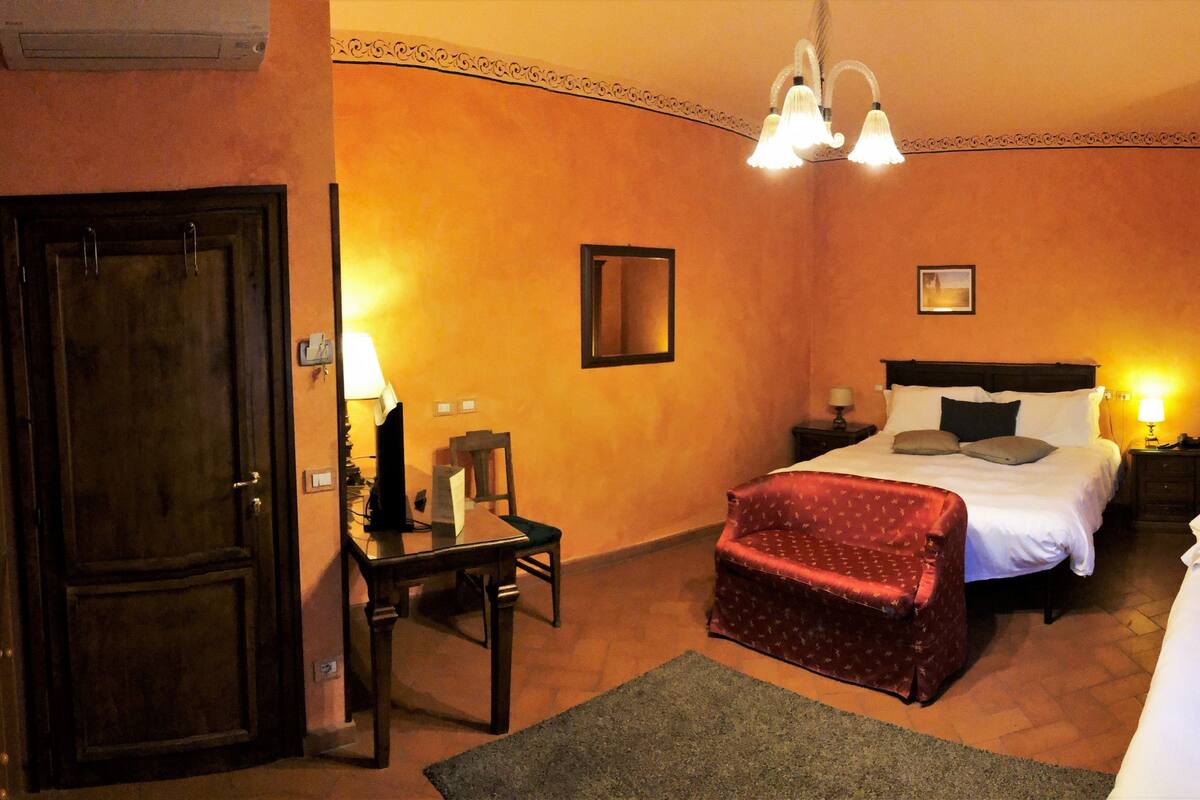 A hotel room with two beds, a desk, a chair, a small table, and a lamp.