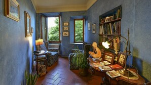 A cozy room with a fireplace, a bookshelf, and a comfortable seating area with a view of the outdoors. - Hotel Bellavista Impruneta (Impruneta)