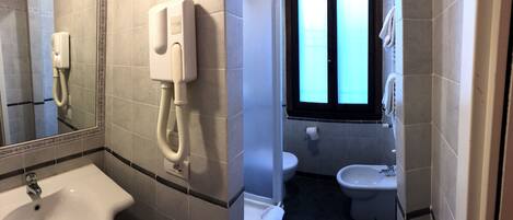 Un baño con lavamanos, inodoro, bidé y un secamanos instalado en la pared.