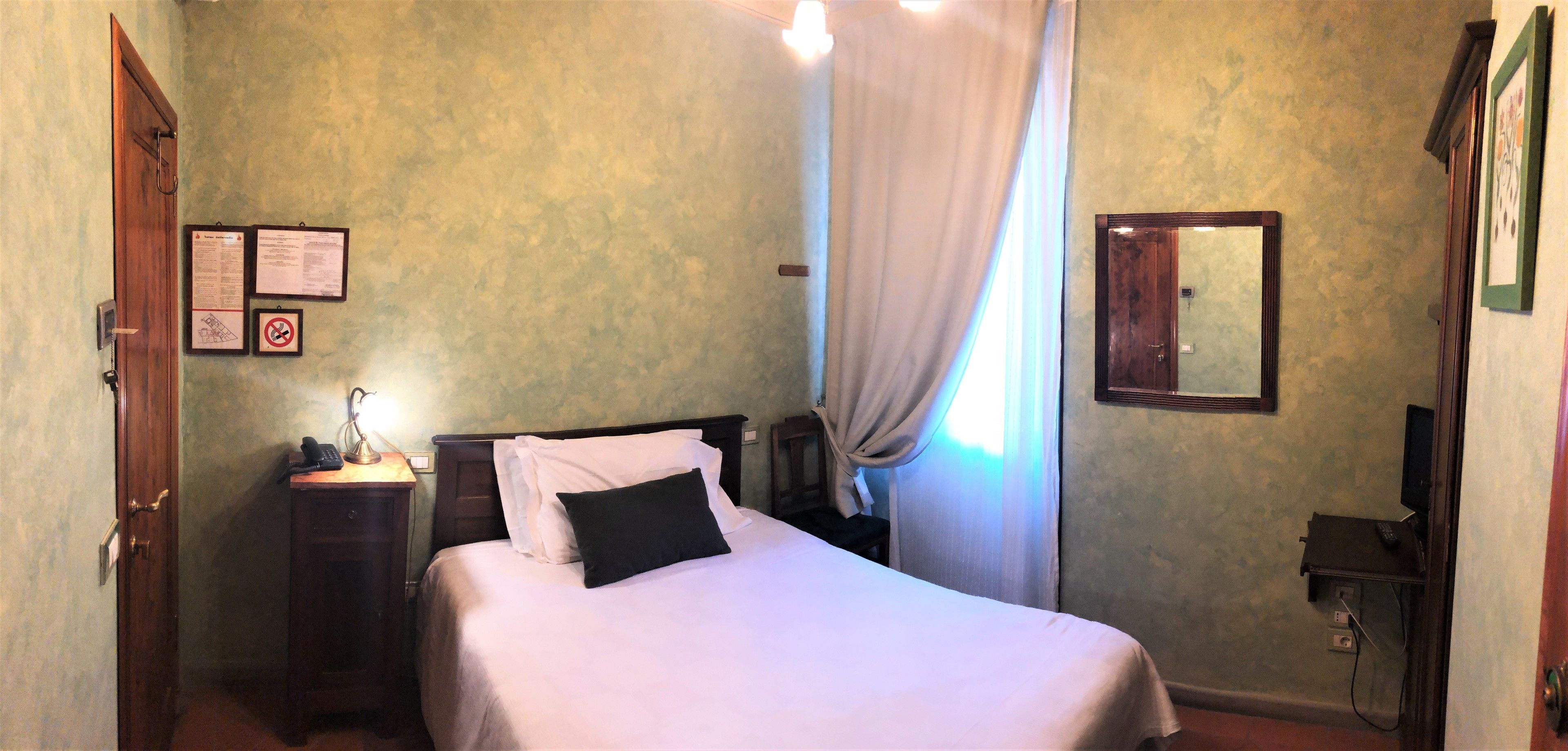 Ein Hotelzimmer mit einem Bett, einem Schreibtisch mit Lampe, einem Spiegel und einer Tür.