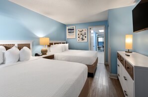 A hotel room with two beds, a nightstand, a lamp, a dresser, and artwork on the walls.