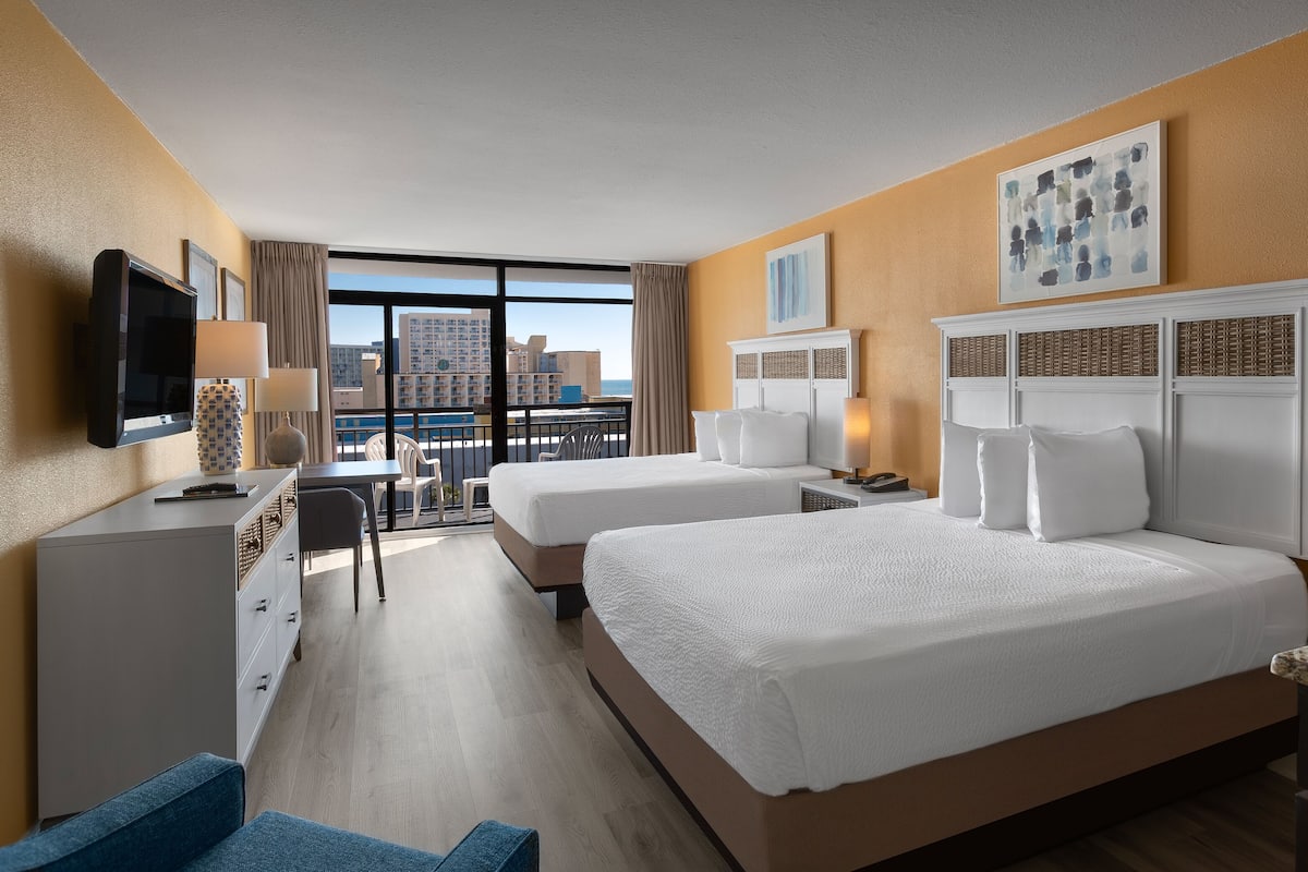 Habitación de hotel con dos camas, un escritorio, una silla, un televisor y un ventanal con vistas a la ciudad.