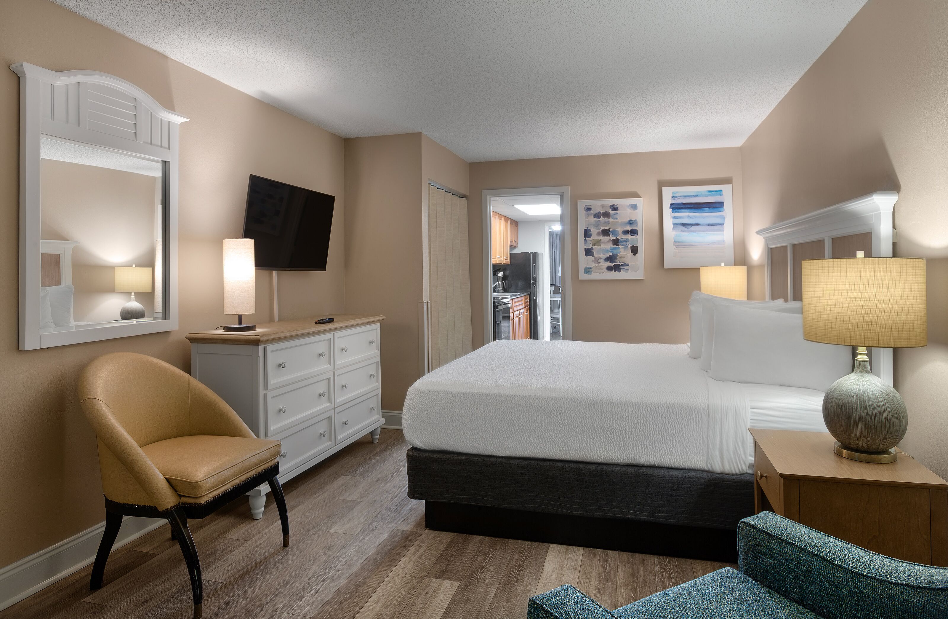 A hotel room with a bed, a chair, a dresser, a television, and artwork on the walls.