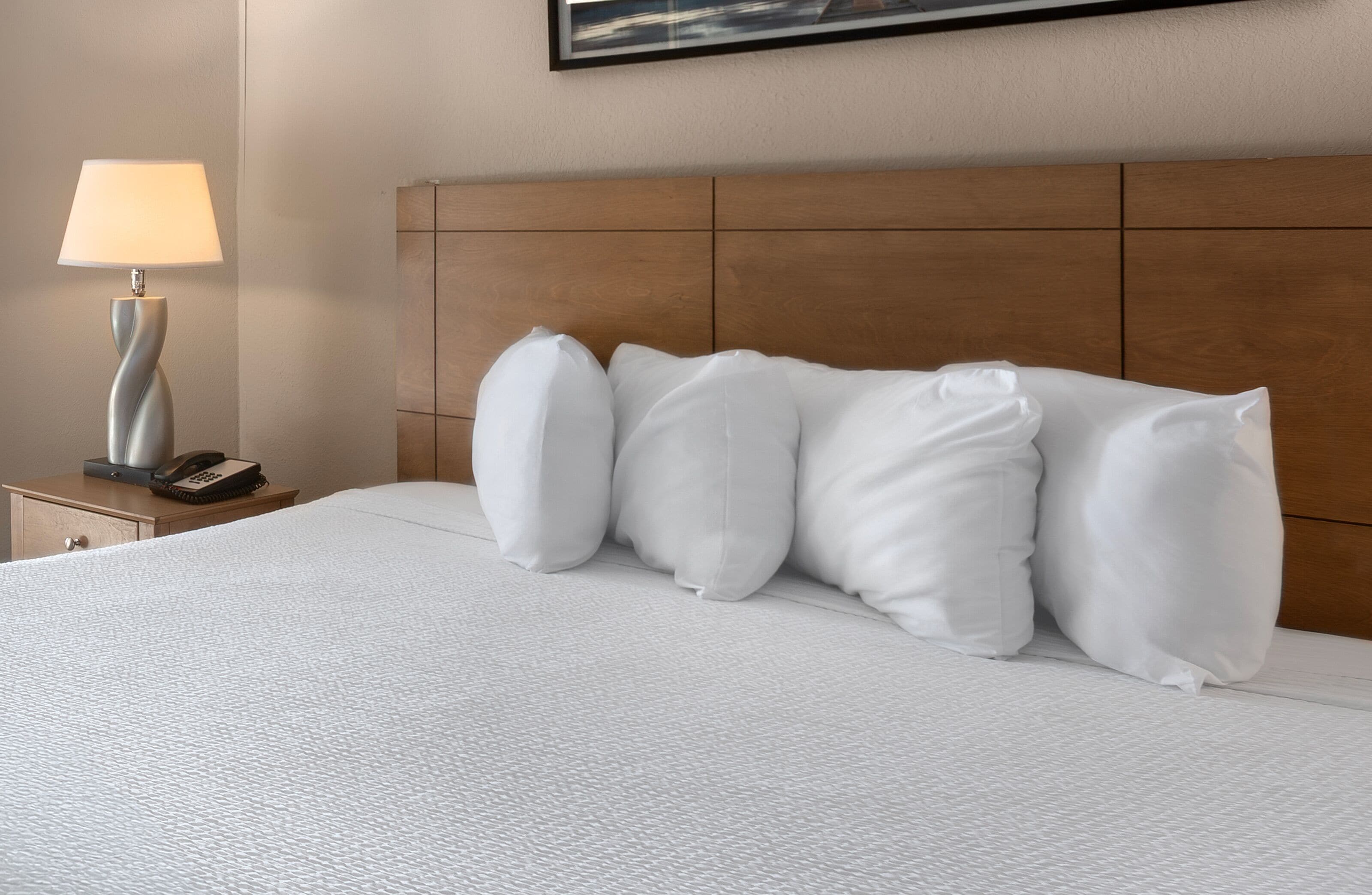 Una camera d'albergo con un letto, cuscini bianchi, una lampada da comodino e un telefono sul tavolino.