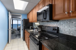 A kitchen with wooden cabinets, a black microwave, a stove, and a tiled backsplash. - Landmark Resort (Myrtle Beach)