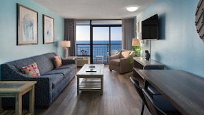 Una habitación de hotel moderna con balcón, un sofá, una mesa de centro, un escritorio y un televisor.