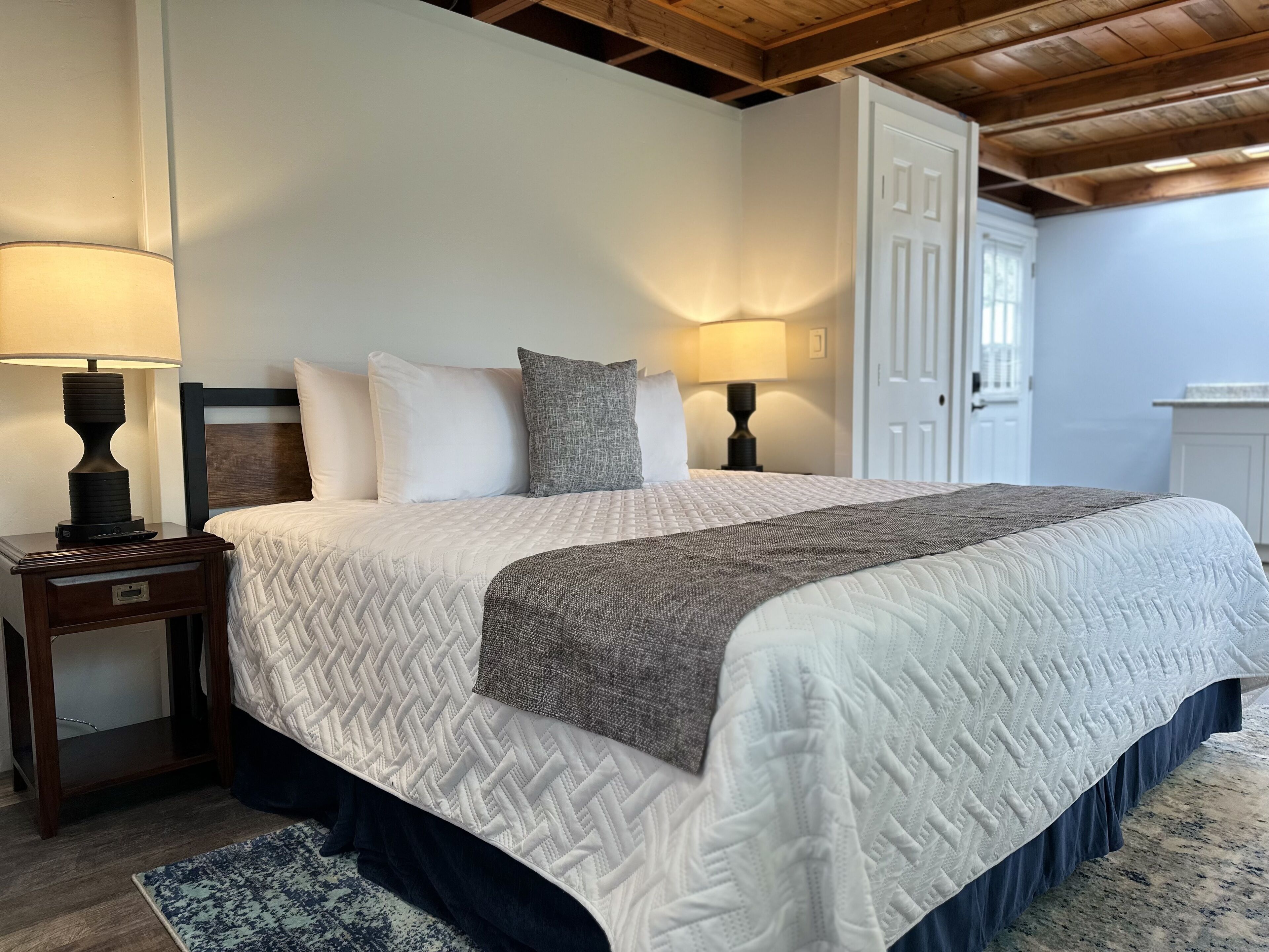 A bedroom with a bed, two bedside tables with lamps, a door, and a window.
