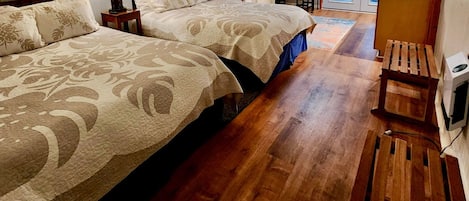 Um quarto acolhedor com duas camas grandes, piso de madeira e um pequeno banco de madeira.