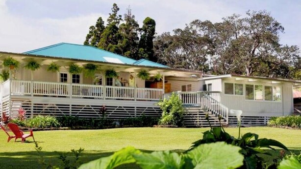 A two-story house with a blue roof, a covered porch, and a small attached structure. - Aloha Junction Guest House (Volcano)