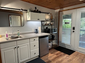 A compact kitchen with a sink, cabinets, a microwave, and a refrigerator. - Aloha Junction Guest House (Volcano)