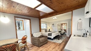 A cozy room with a wooden ceiling, a dining table with chairs, a sofa, and a bed with a mirror. - Aloha Junction Guest House (Volcano)