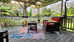 A covered porch with wicker furniture, a table, and potted plants. - Aloha Junction Guest House (Volcano)
