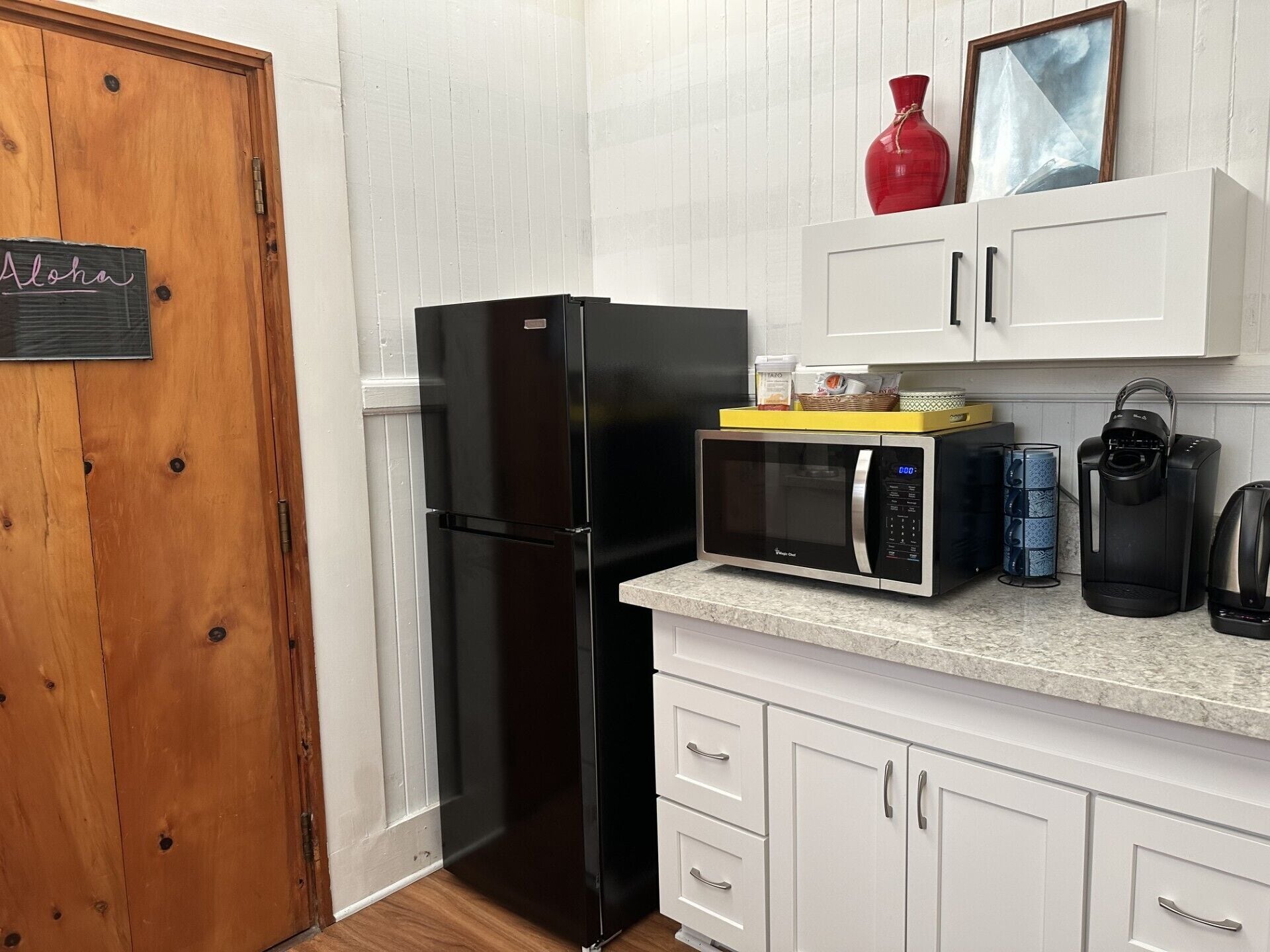 A compact kitchen with a black refrigerator, a microwave, a kettle, and a coffee maker.