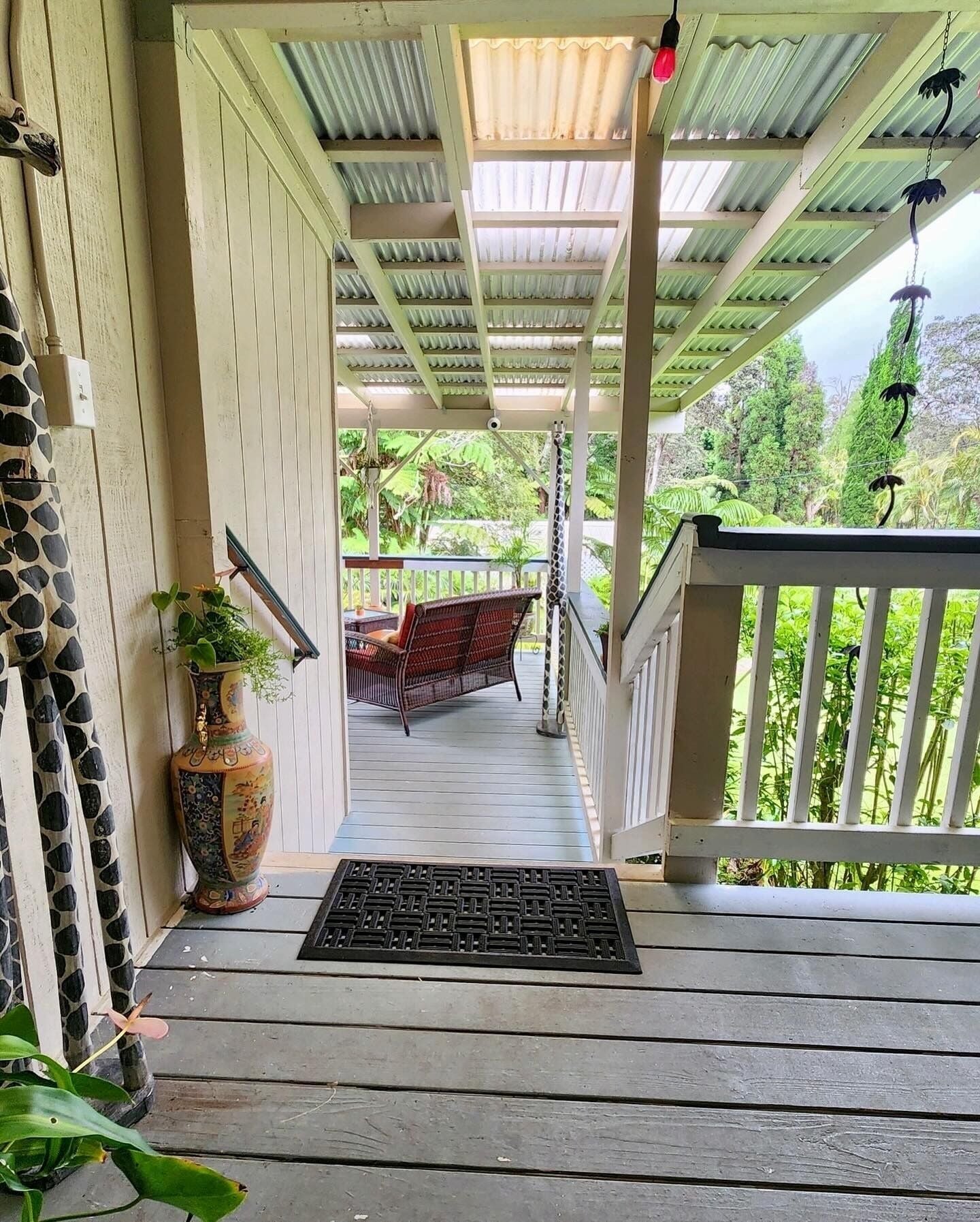 A covered porch with a wooden floor, a bench, and a potted plant.