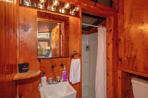 A wooden bathroom with a sink, mirror, and shower curtain. - Aloha Junction Bed and Breakfast (Volcano)