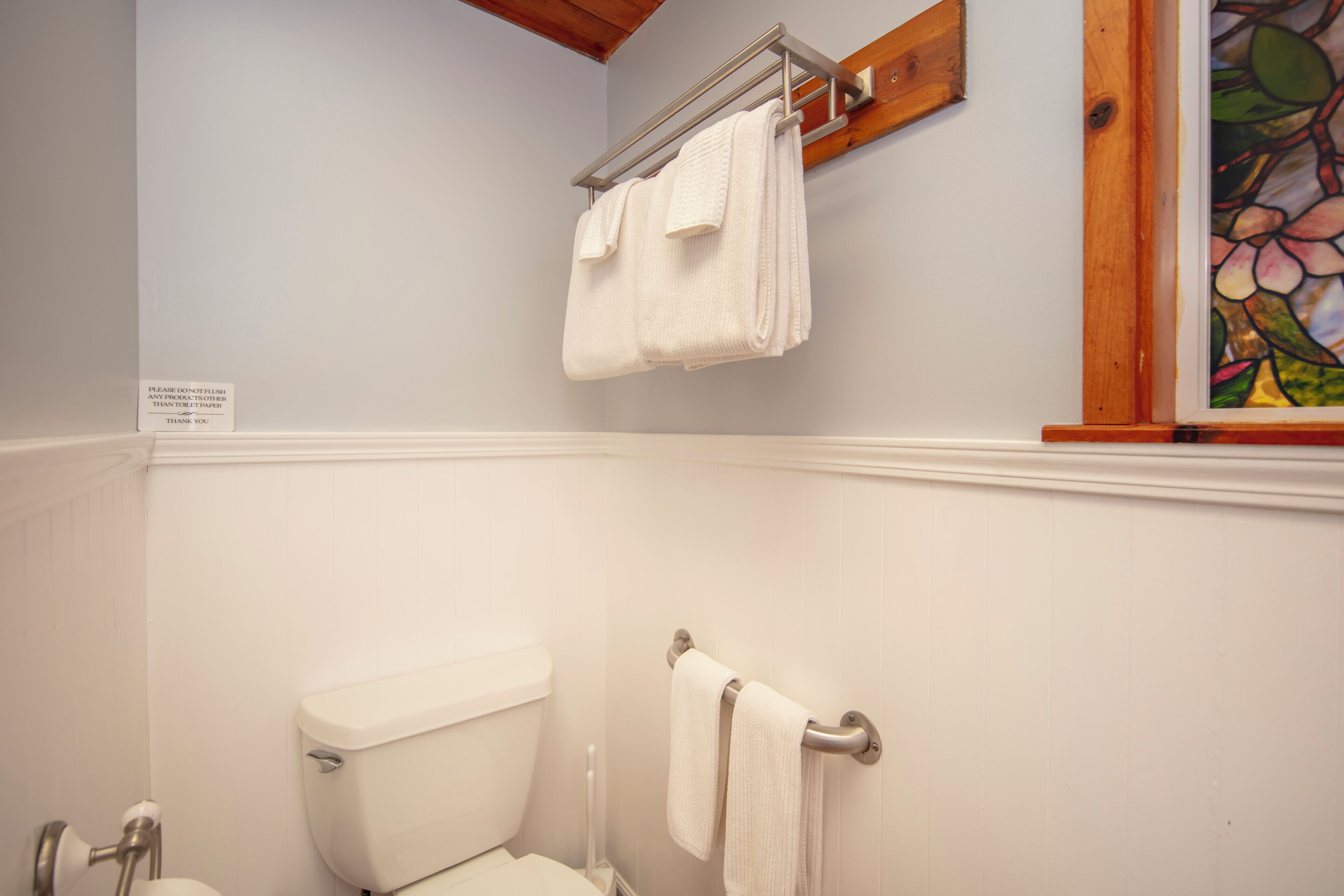 A bathroom with white walls, a toilet, a sink, and two towel racks with folded towels.