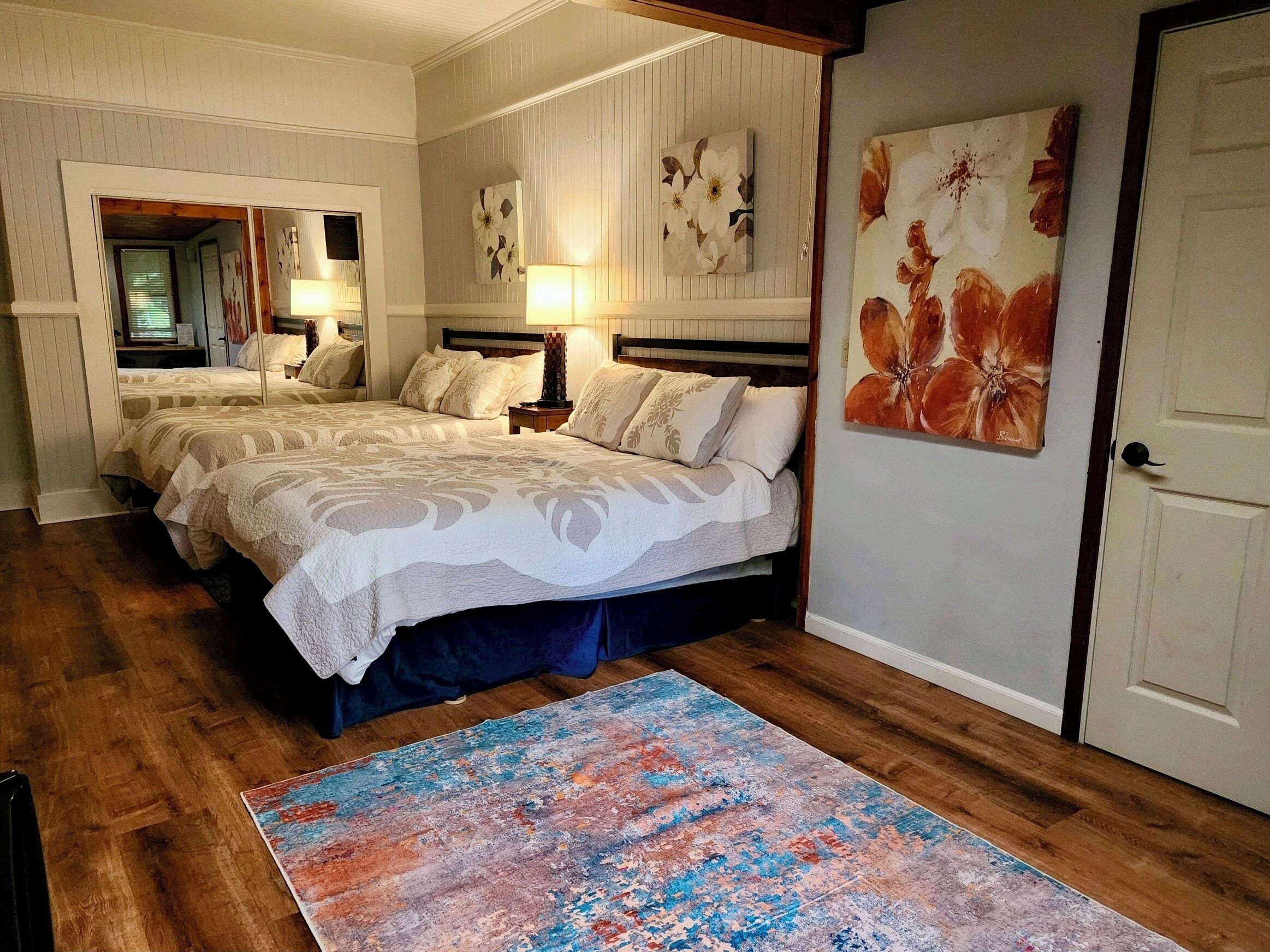 A bedroom with two beds, a large abstract rug, and floral artwork on the walls.
