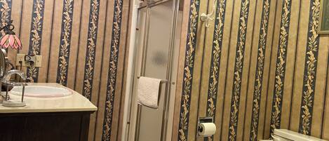 A bathroom with striped wallpaper, a sink with a pink faucet, a shower with a glass door, and a toilet.