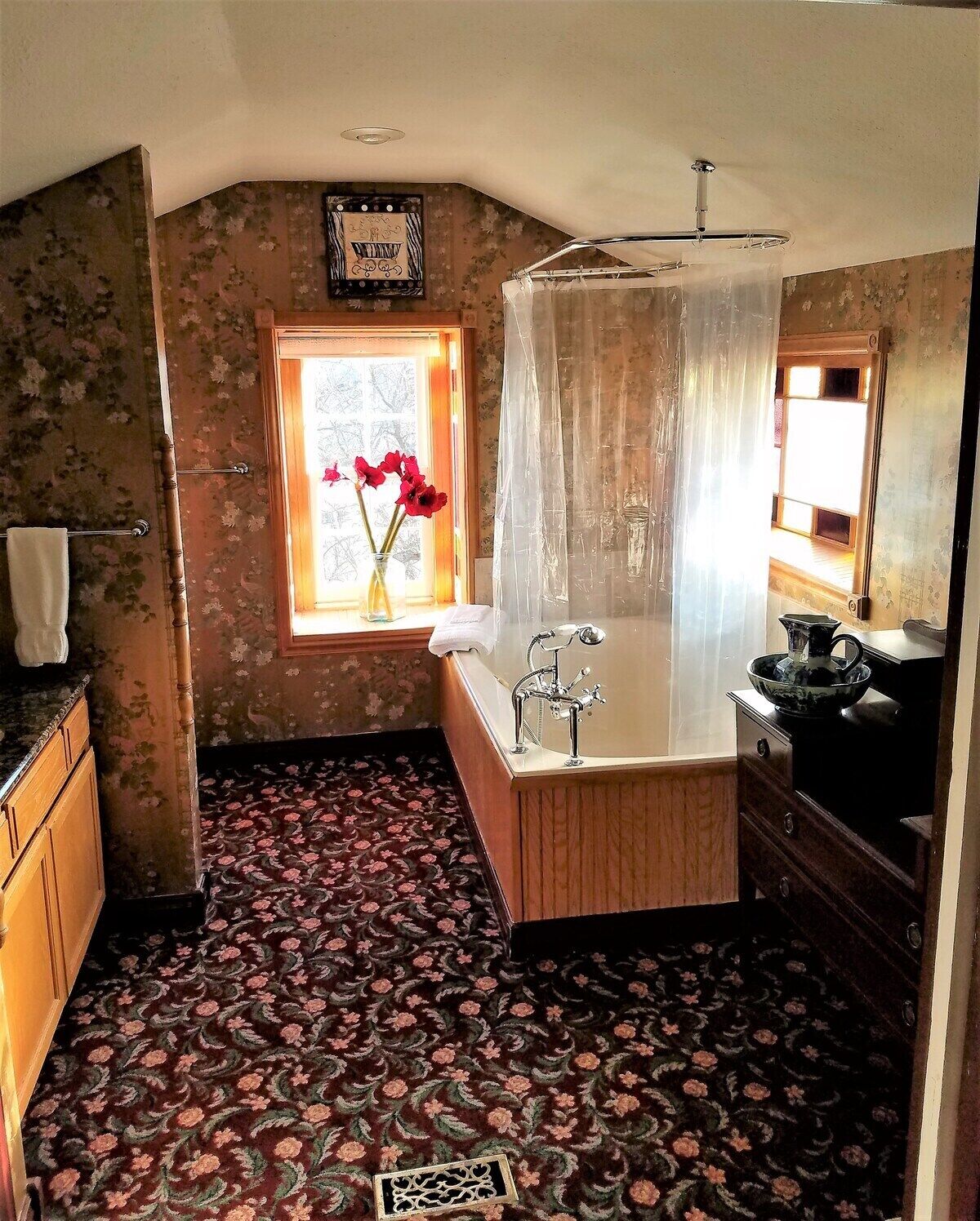 A bathroom with a bathtub, a shower, and a window with flowers.