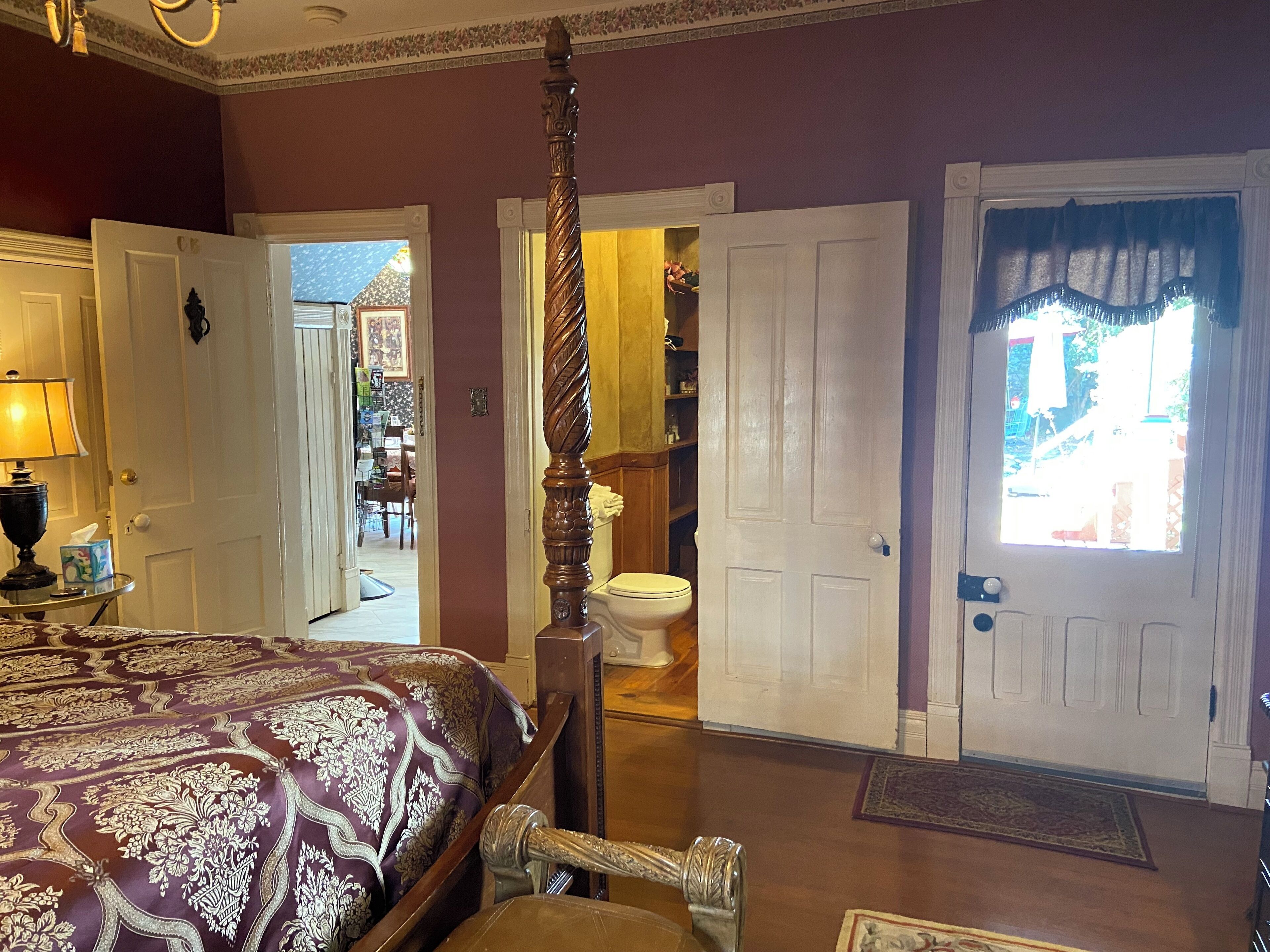 A bedroom with a four-poster bed, a chandelier, and a view of the bathroom through an open door.