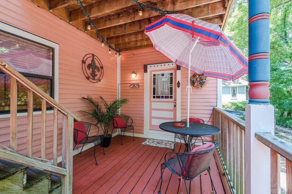 A covered porch with a wooden staircase, a table with chairs, and a decorative umbrella.