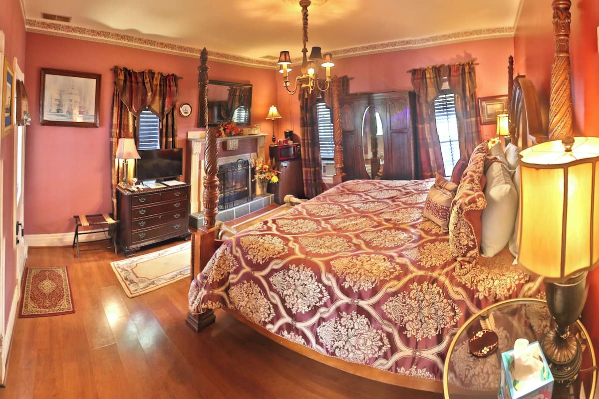 A bedroom with a large bed, a dresser, a television, a fireplace, and a chandelier.