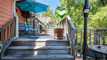 A wooden deck with steps leading to a covered patio area, a table with chairs, and a large potted plant.
