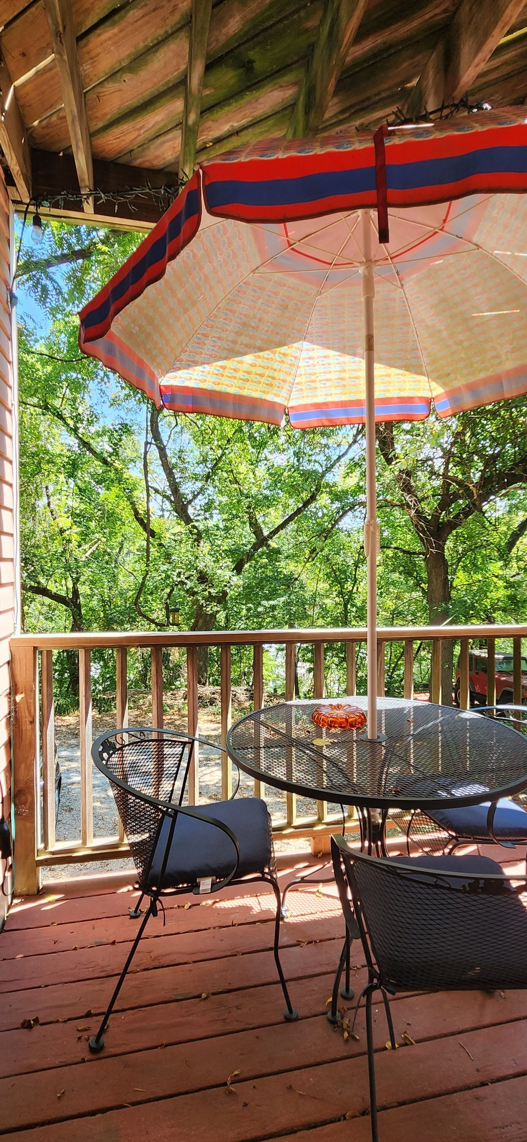 A covered outdoor area with a table and chairs, surrounded by trees.