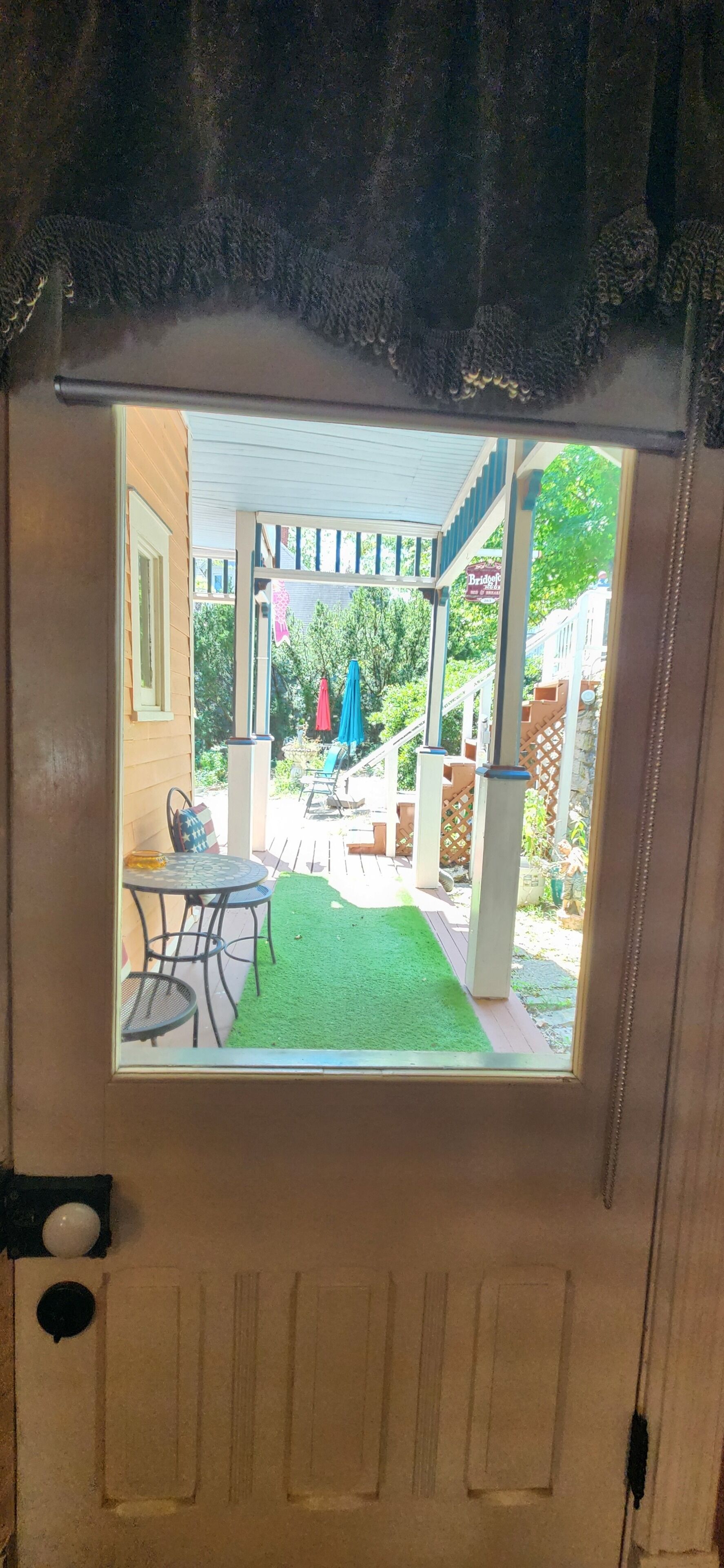 A view through a door of a covered outdoor area with a table and chairs, a green lawn, and a building in the background.