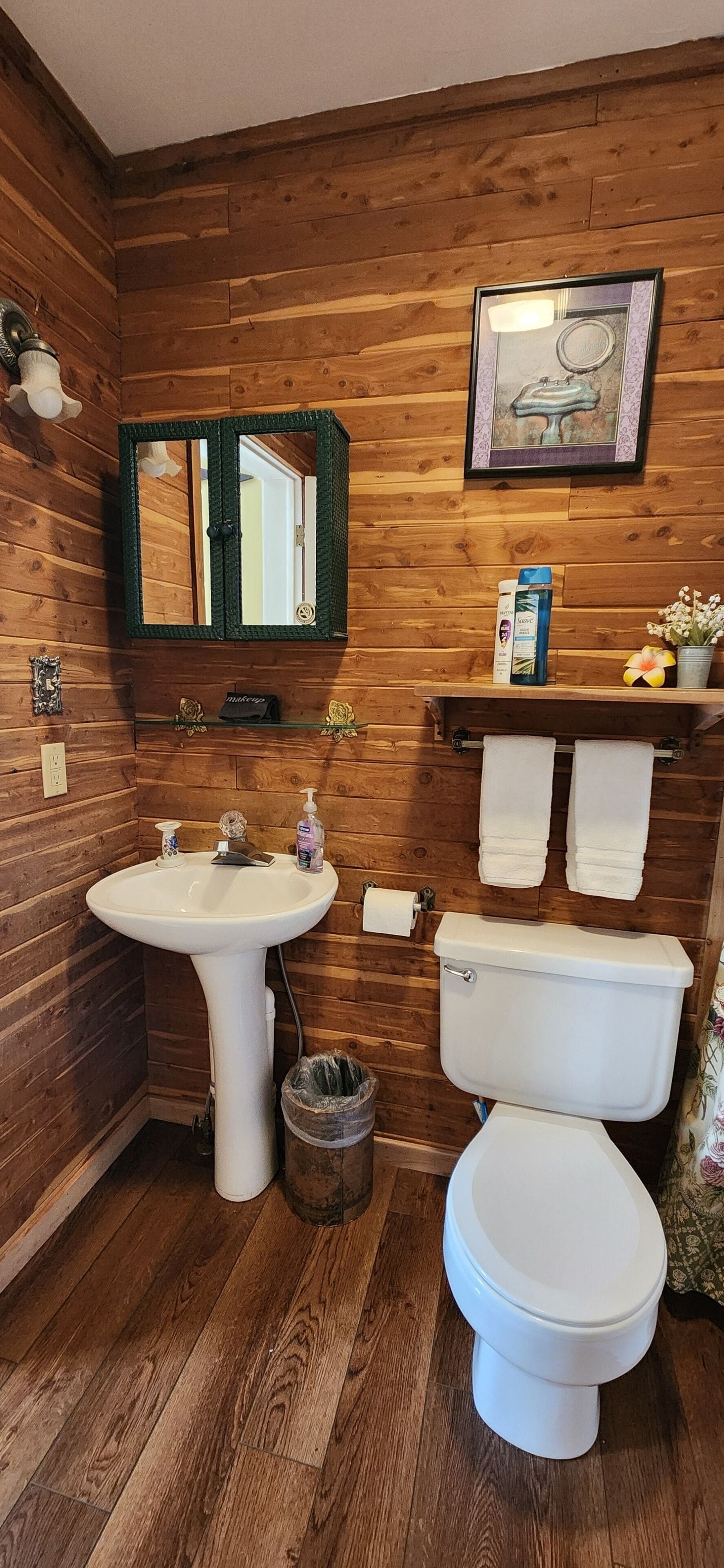 A bathroom with wooden paneling, a white sink, a toilet, a mirror, and a shelf with toiletries.