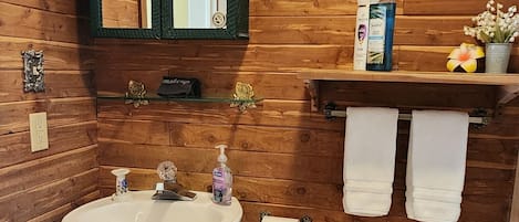 A bathroom with wooden paneling, a white sink, a toilet, a mirror, and a shelf with toiletries.