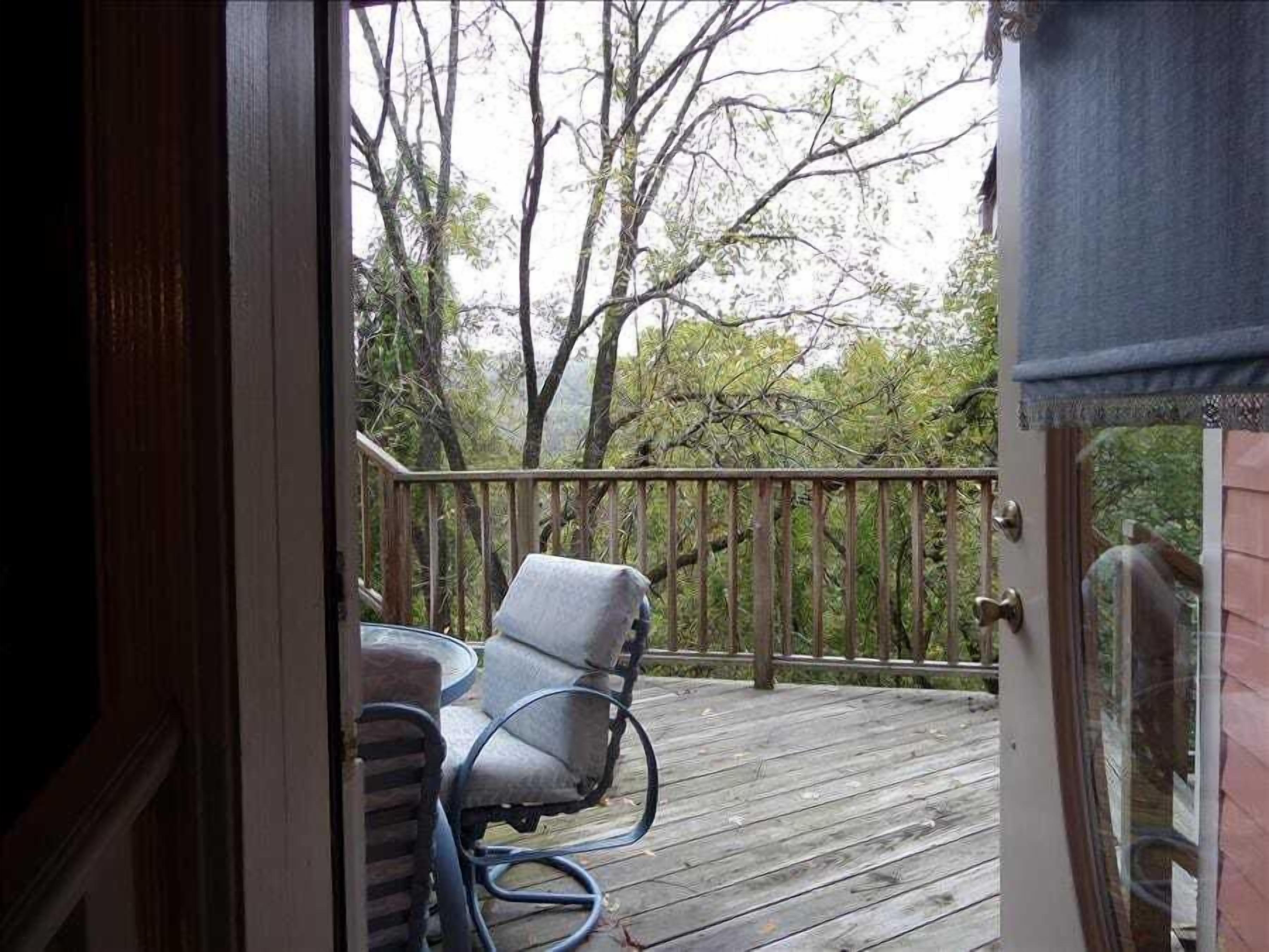 A wooden deck with two chairs and a table, overlooking a forested area.