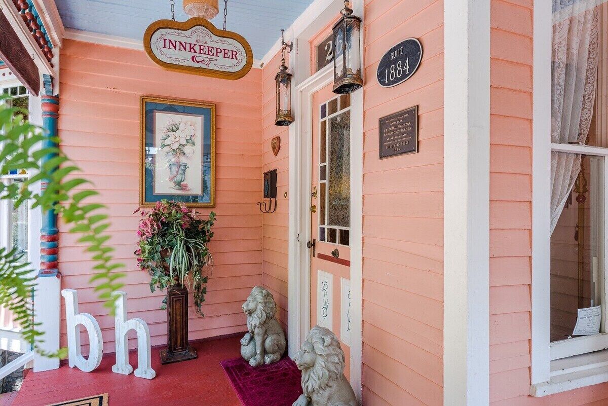A pink building with a sign reading "Innkeeper" and a plaque indicating it was built in 1884. There are two stone lion statues on the porch.