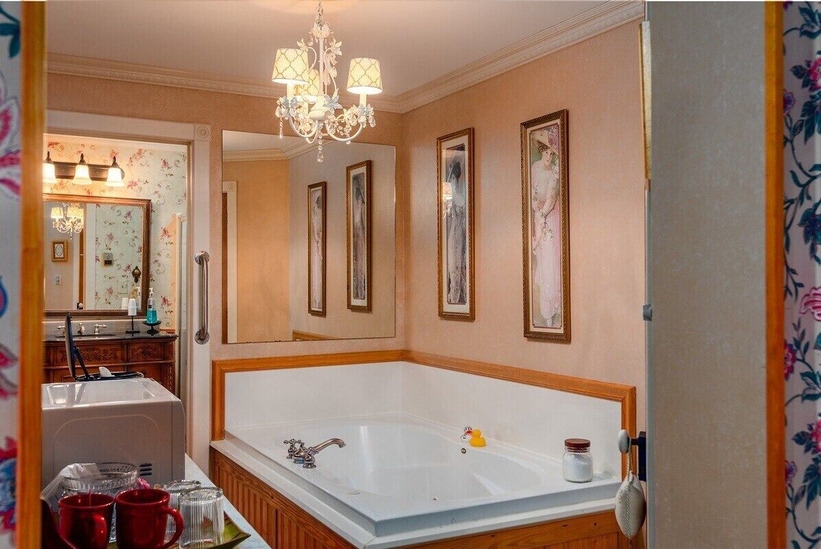 Un baño con una bañera grande, un candelabro, obras de arte enmarcadas en las paredes y un espejo con papel tapiz floral.