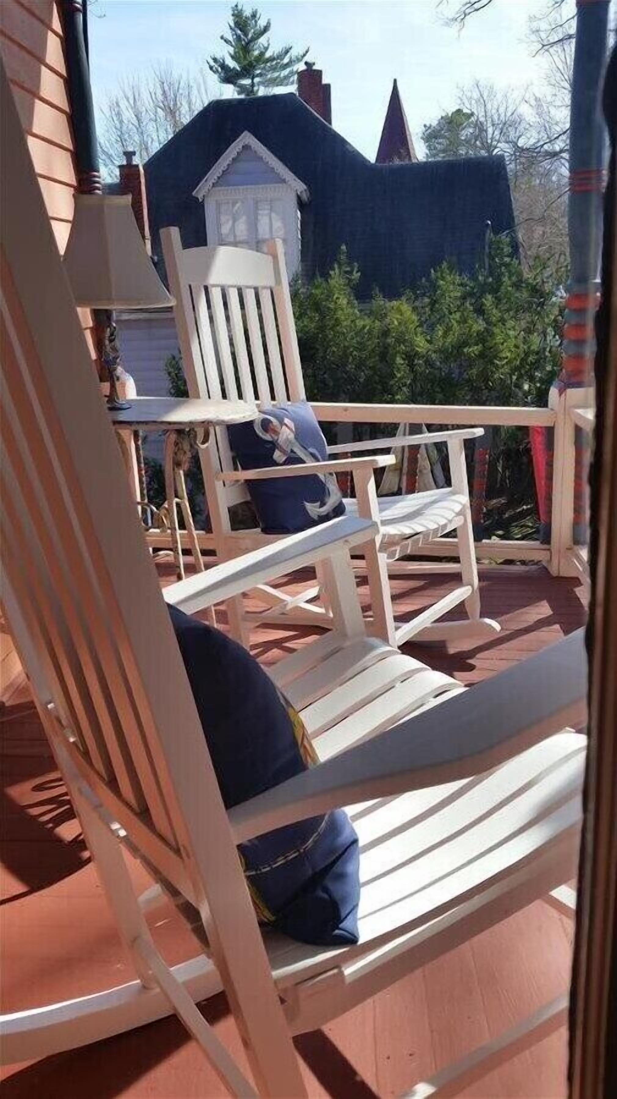 A wooden deck with two Adirondack chairs, one with a blue cushion.