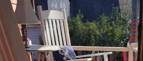 A wooden deck with two Adirondack chairs, one with a blue cushion.