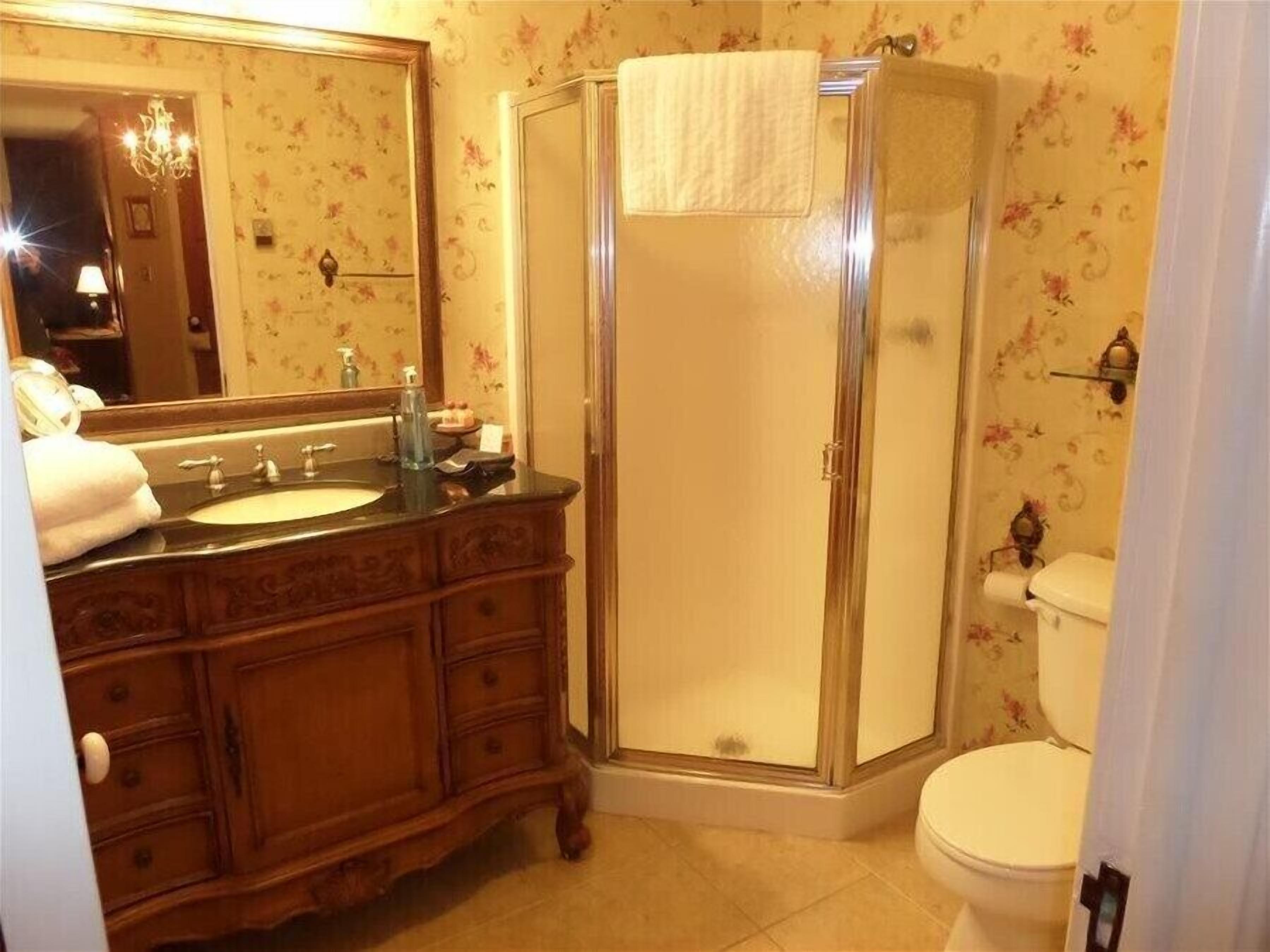 A bathroom with a wooden vanity, a glass shower enclosure, and a toilet.