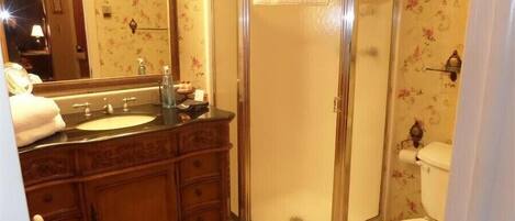 Een badkamer met een houten wastafelmeubel, een douchecabine met glazen wanden en een toilet.