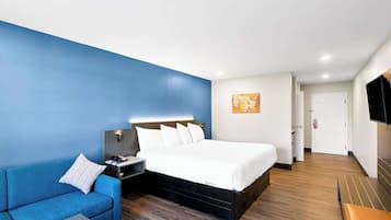 Ein Hotelzimmer mit einem Bett, einem blauen Sofa, einem Nachttisch mit Lampe, einem Flachbildfernseher und Holzböden.