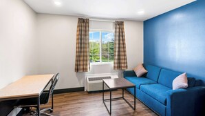 A room with a desk, a blue sofa, a window with curtains, and a radiator. - Econo Lodge Bethel - Danbury (Bethel)
