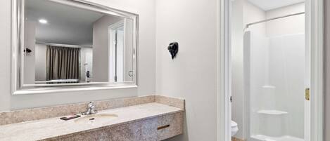 Un baño moderno con lavamanos de encimera de granito, un espejo grande y una ducha a ras de suelo.