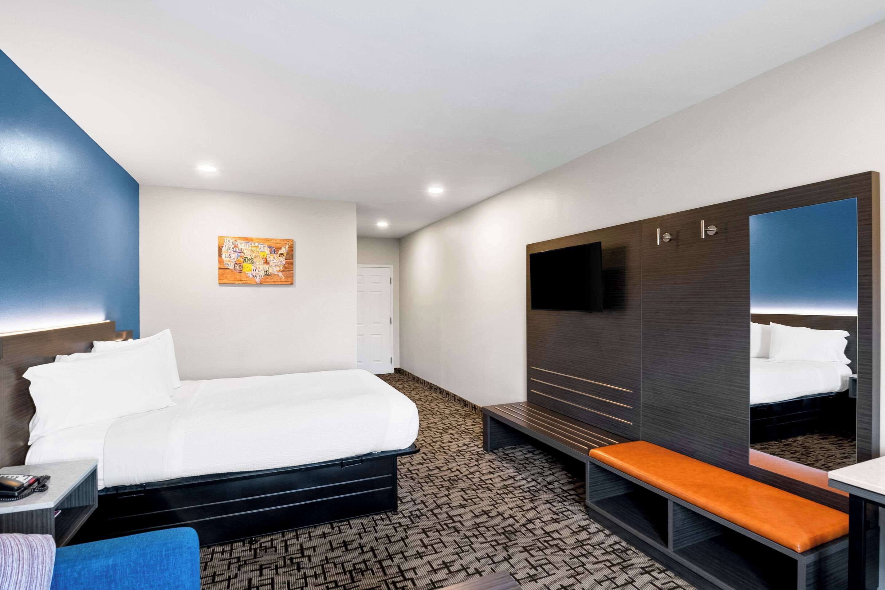 Habitación de hotel con cama, banca, armario, televisor y una obra de arte colgada en la pared.