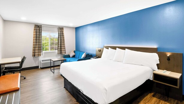 A hotel room with a large bed, a desk, a chair, a sofa, and a window with curtains. - Econo Lodge Bethel - Danbury (Bethel)